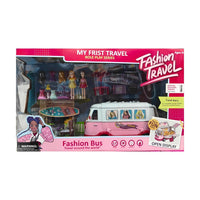 A smiling young girl with blonde hair is lying on her stomach, looking at a pink and white toy bus. Spread around the bus are a small doll in a yellow dress, a helicopter toy, a pink beach chair, a small table with an umbrella, and other small accessories. The background is a soft pink and white.